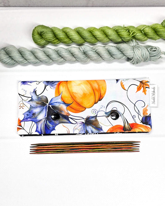 Nadelgarage für 15 cm lange Nadelspiele mit zwei schwarzen Druckknöpfen, großen orangefarbenen Kürbissen und blau-violetten Herbstblättern auf weißem Stoff. Handgenäht in Bayern von Nadelmikado.