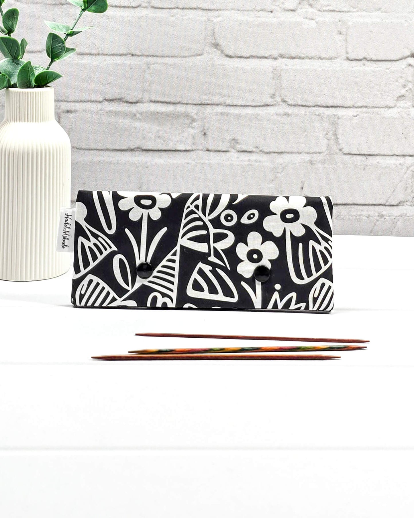 Nadelgarage für 15 cm lange Nadelspiele sichert Sockenstricknadeln und schützt das Strickzeug vor dem Herunterrutschen der Maschen. Grafisches Motiv mit schwarz-weißen Scandi-Blumen. Handgenäht in Bayern von Nadelmikado