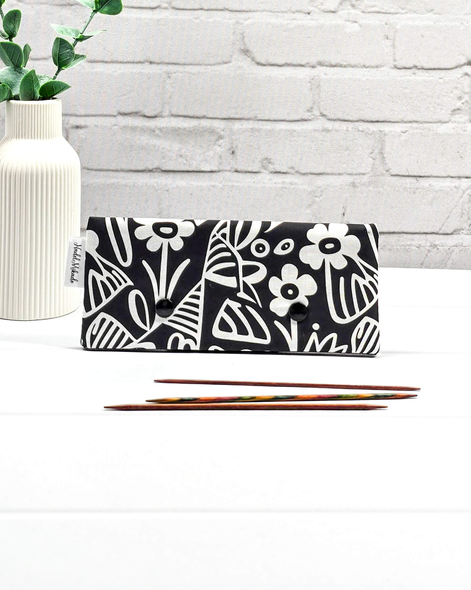Nadelgarage für 15 cm lange Nadelspiele sichert Sockenstricknadeln und schützt das Strickzeug vor dem Herunterrutschen der Maschen. Grafisches Motiv mit schwarz-weißen Scandi-Blumen. Handgenäht in Bayern von Nadelmikado