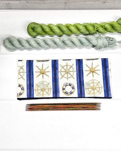 Nadelgarage für 15cm Nadelspiele aus cremeweißem Stoff mit blauen Längsstreifen, maritimen Motiven wie Kompassrosen und Rettungsringen sowie zwei hellgrauen Druckknöpfen. Handgenäht in Bayern von Nadelmikado. 