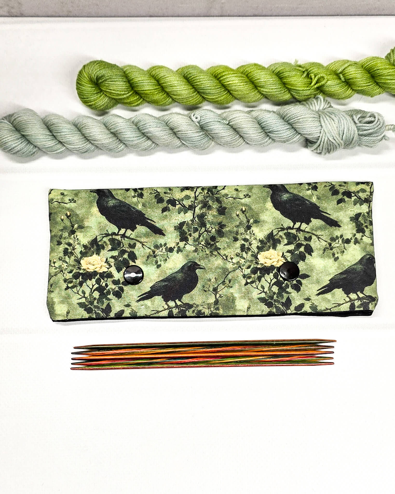 Grüne Nadelgarage mit Druckknöpfen, gemustert mit Raben und Rosen, passend für ein 15cm Nadelspiel zum Schutz der Sockenmaschen. Handgenäht in Bayern von Nadelmikado.