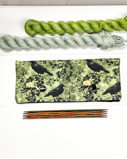 Grüne Nadelgarage mit Druckknöpfen, gemustert mit Raben und Rosen, passend für ein 15cm Nadelspiel zum Schutz der Sockenmaschen. Handgenäht in Bayern von Nadelmikado.