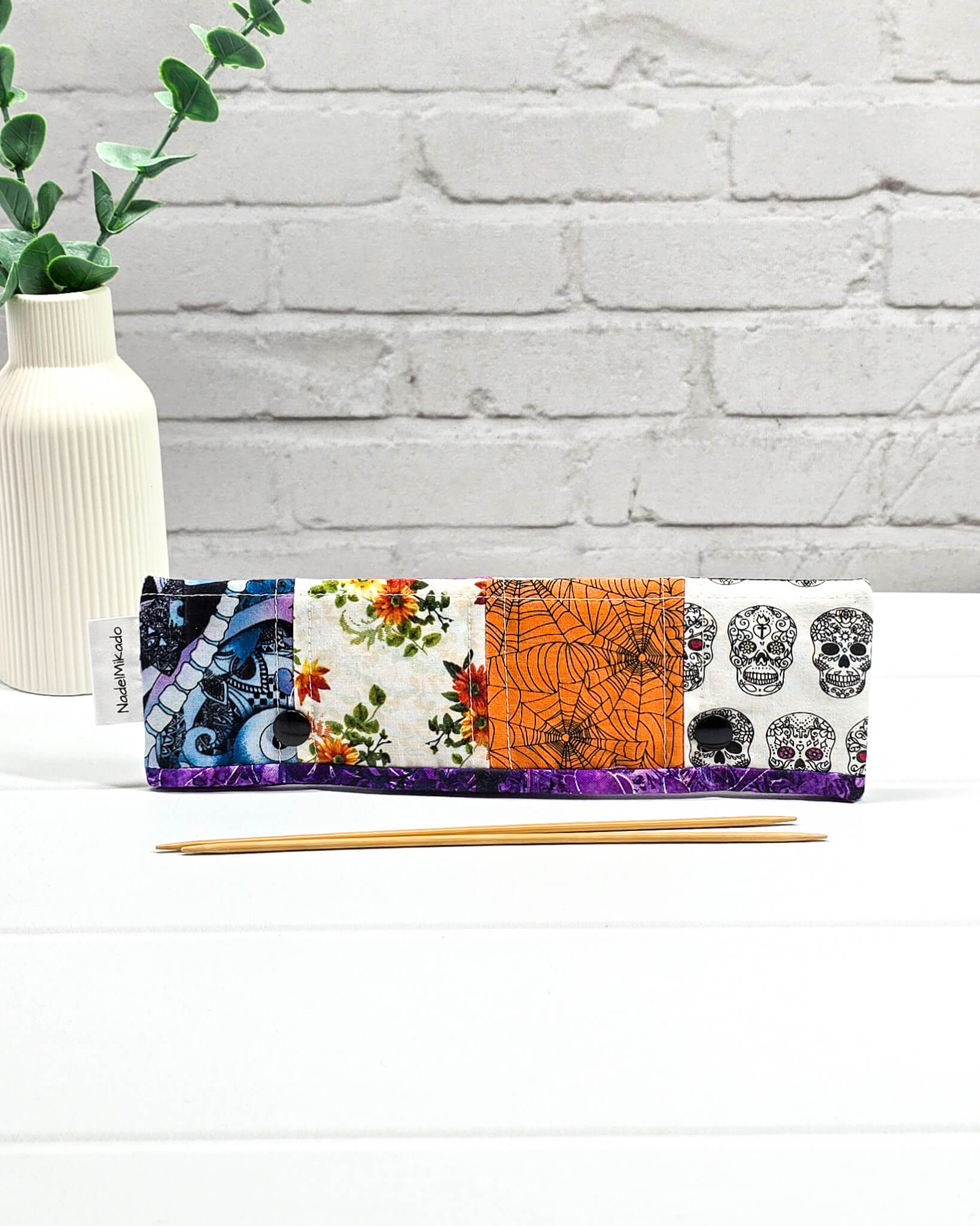 Nadelgarage für 20 cm Nadelspiele im Patchwork-Design mit Totenköpfen, Spinnennetzen auf Orange und floralen Mustern sowie schwarzen Druckknöpfen. Handgenäht in Bayern von Nadelmikado.