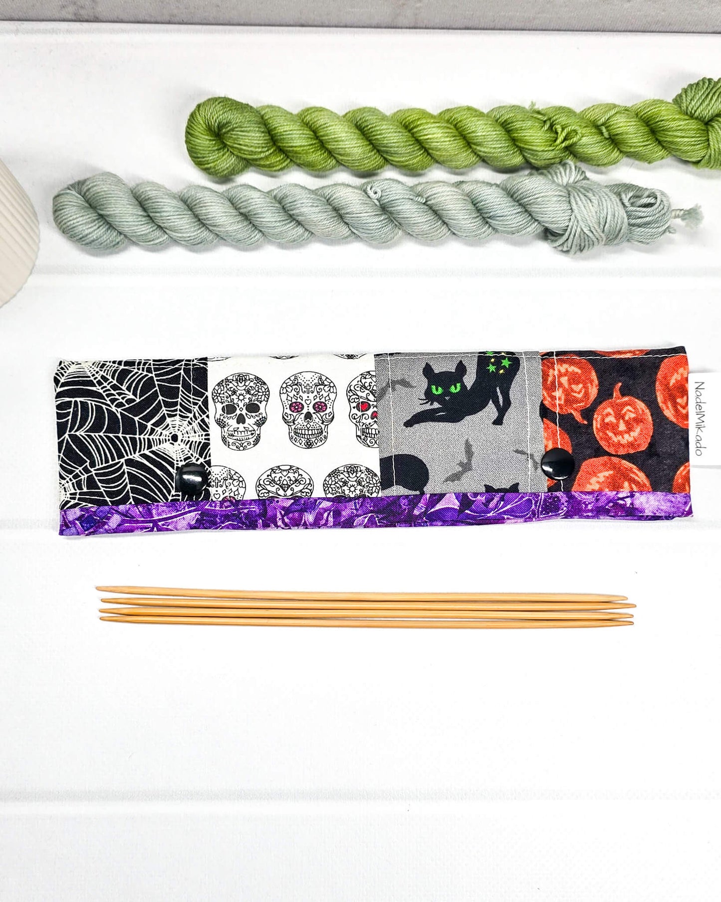 Nadelgarage für 20 cm Nadelspiele im Patchwork-Look mit Spinnennetzen, Totenköpfen, einer schwarzen Katze und Halloween-Kürbissen sowie schwarzen Druckknöpfen. Handgenäht in Bayern von Nadelmikado.