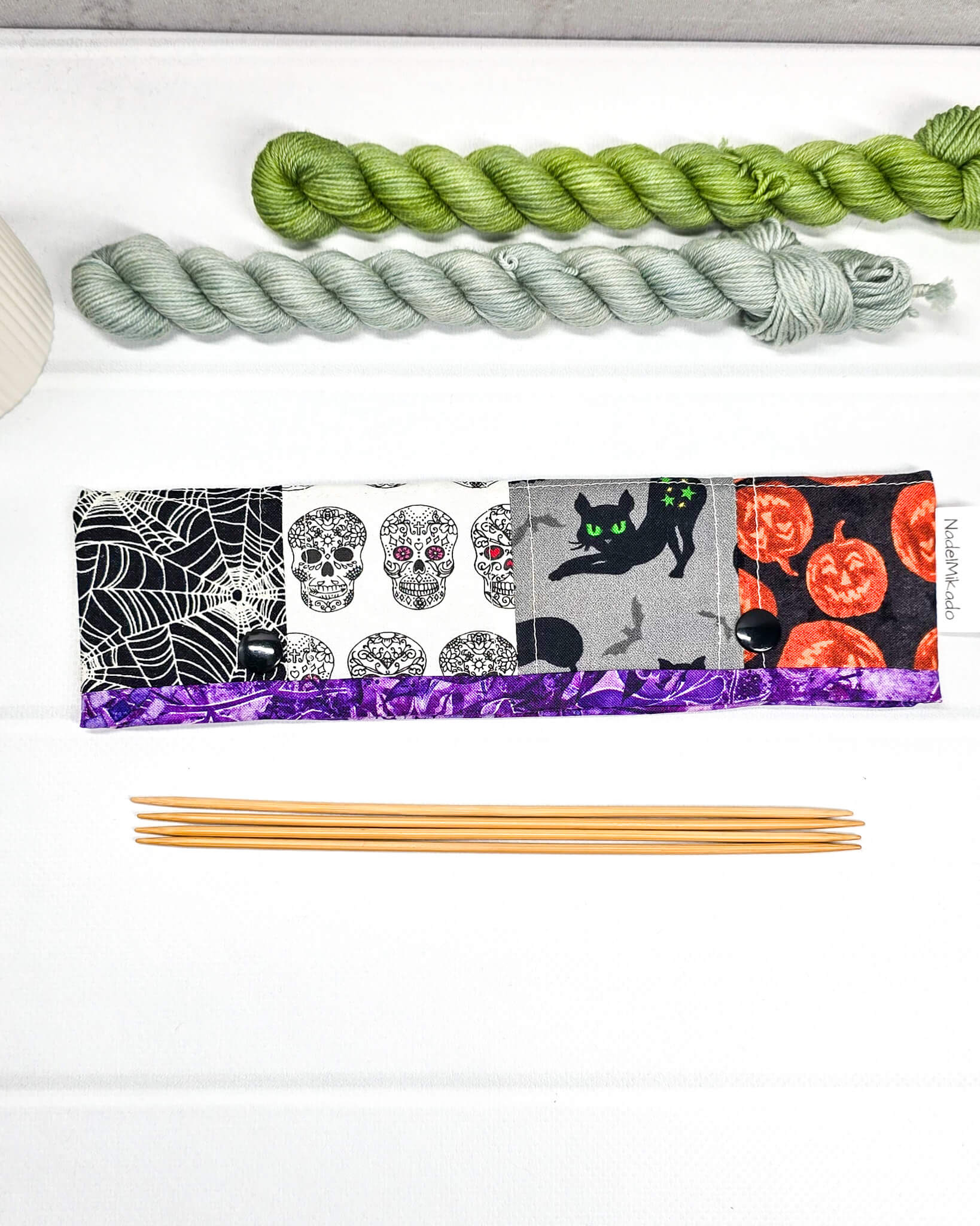 Nadelgarage für 20 cm Nadelspiele im Patchwork-Look mit Spinnennetzen, Totenköpfen, einer schwarzen Katze und Halloween-Kürbissen sowie schwarzen Druckknöpfen. Handgenäht in Bayern von Nadelmikado.