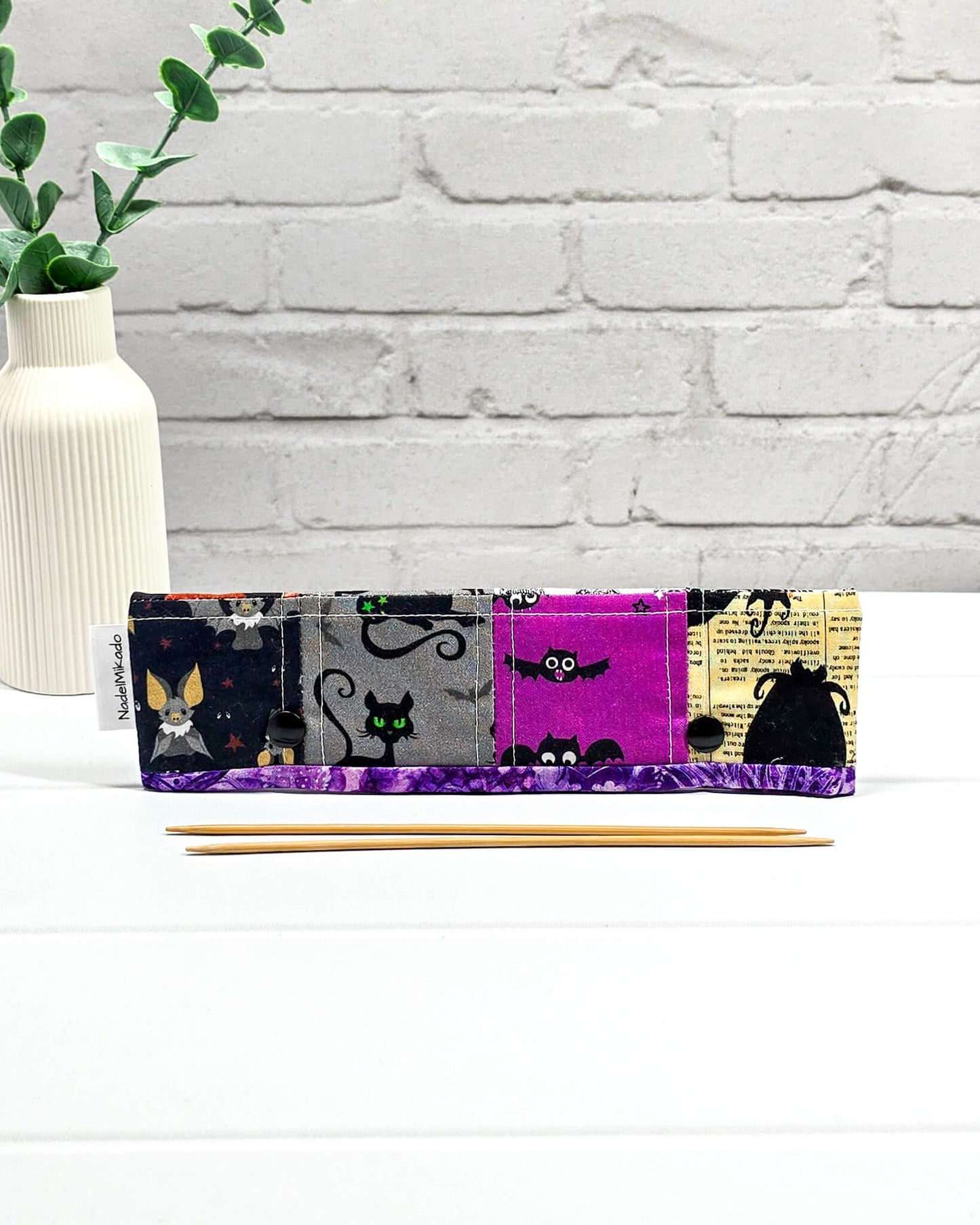 Nadelgarage für 20 cm Nadelspiele im Patchwork-Look mit Spinnennetzen, Totenköpfen, einer schwarzen Katze und Halloween-Kürbissen sowie schwarzen Druckknöpfen. Handgenäht in Bayern von Nadelmikado.