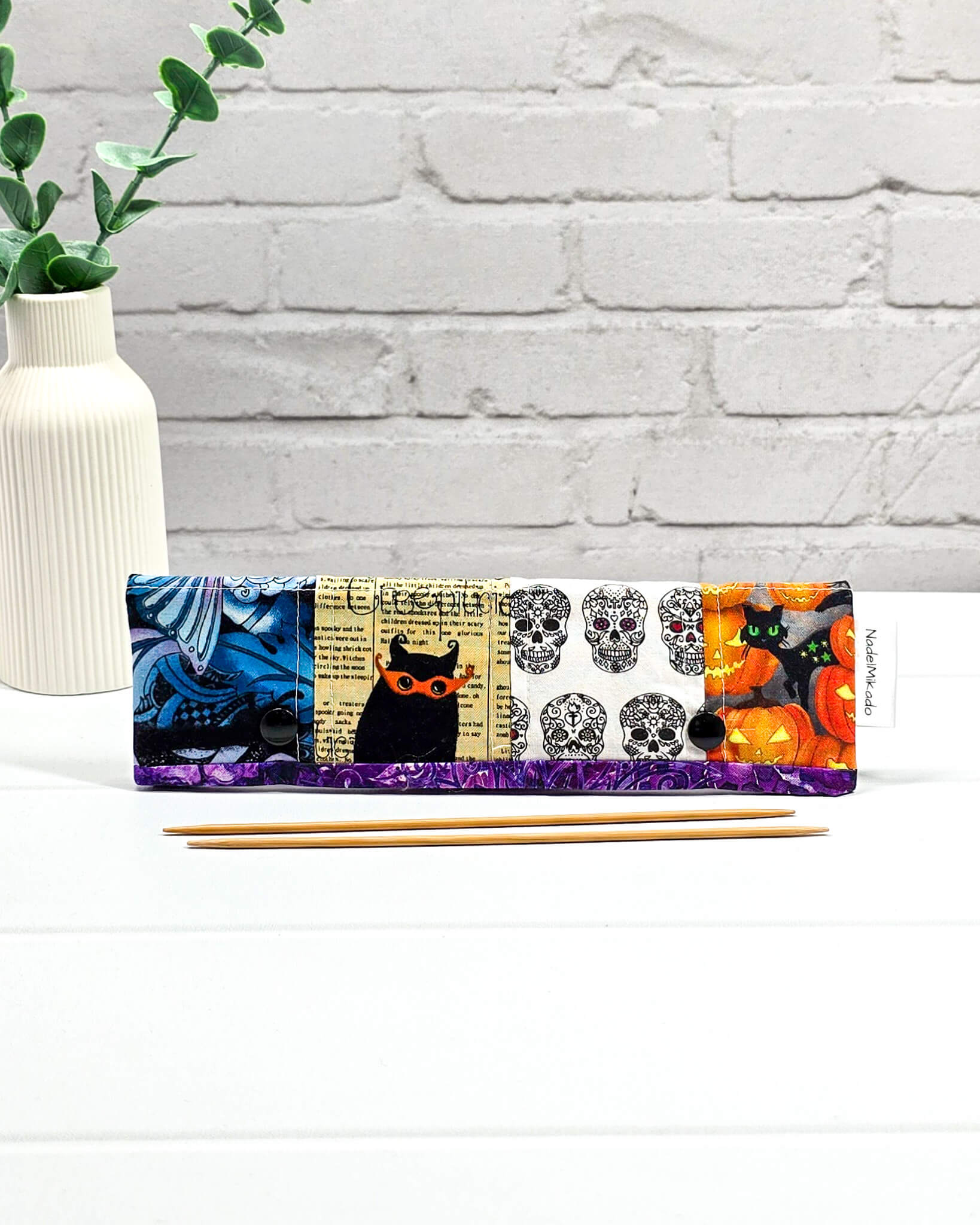 Nadelgarage für 20 cm Nadelspiele im Patchwork-Stil mit Motiven von Totenköpfen, Kürbissen und abstrakten violetten Mustern sowie schwarzen Druckknöpfen. Handgenäht in Bayern von Nadelmikado