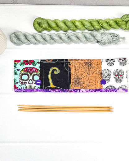 Nadelgarage für 20 cm Nadelspiele im Patchwork-Design mit Motiven von Spinnennetzen, einer schwarzen Katze und herbstlichen Blumen sowie lila Druckknöpfen. Handgenäht in Bayern von Nadelmikado.