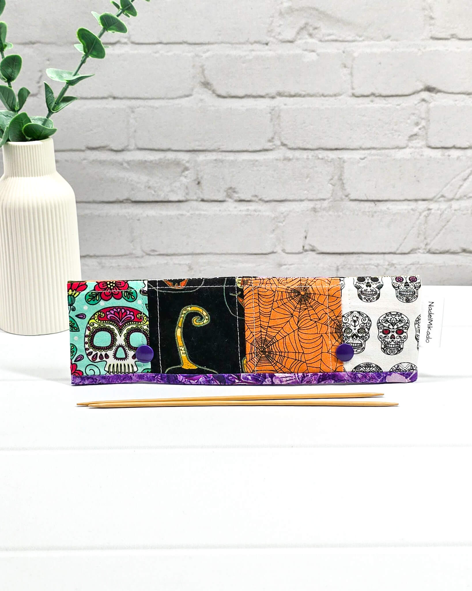 Nadelgarage für 20 cm Nadelspiele im Patchwork-Design mit Motiven von Spinnennetzen, einer schwarzen Katze und herbstlichen Blumen sowie lila Druckknöpfen. Handgenäht in Bayern von Nadelmikado.