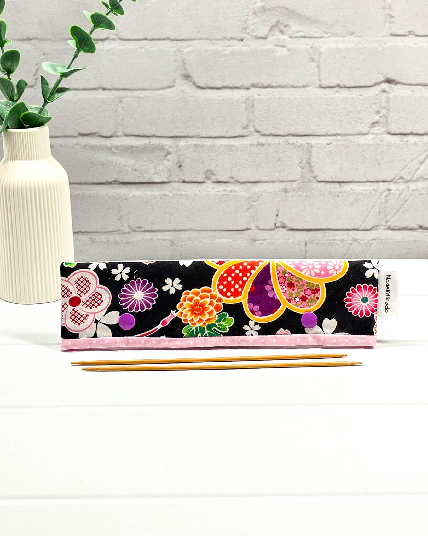 Nadelgarage für 20 cm Nadelspiele mit großen bunten Blumenmotiven im japanischen Stil auf schwarzem Stoff und lila Druckknöpfen. Handgenäht in Bayern von Nadelmikado.