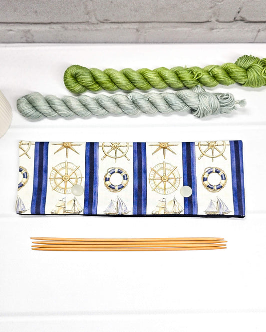 Nadelgarage für 20cm Nadelspiele aus cremeweißem Stoff mit blauen Längsstreifen, maritimen Motiven wie Steuerrädern und Schiffen sowie zwei hellen Druckknöpfen. Handgenäht in Bayern von Nadelmikado. 