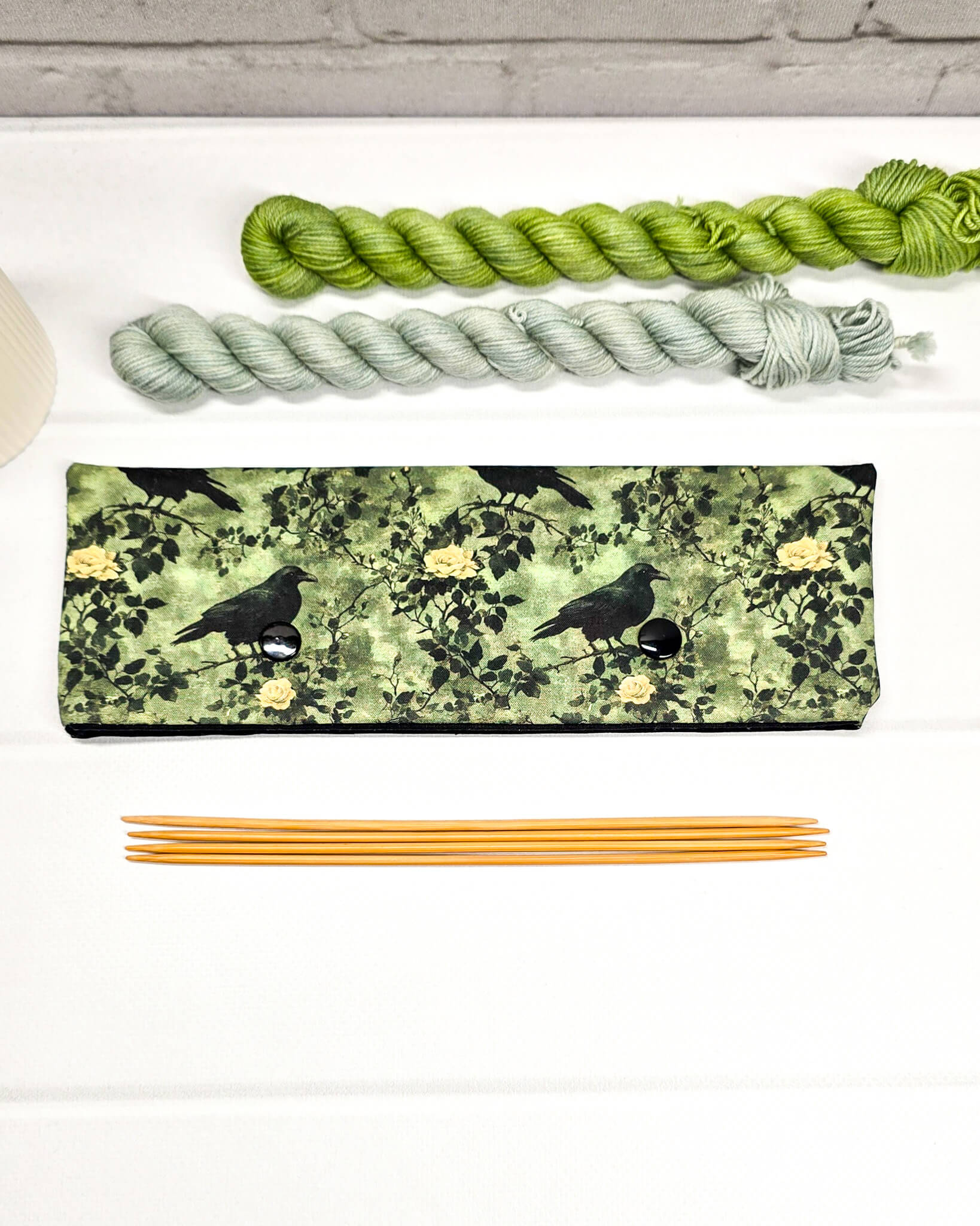 Lange grüne Nadelgarage mit Druckknöpfen, gemustert mit Raben und Rosen, passend für ein 20cm Nadelspiel zum Schutz von Strickmaschen. Handgenäht von Nadelmikado in Bayern.