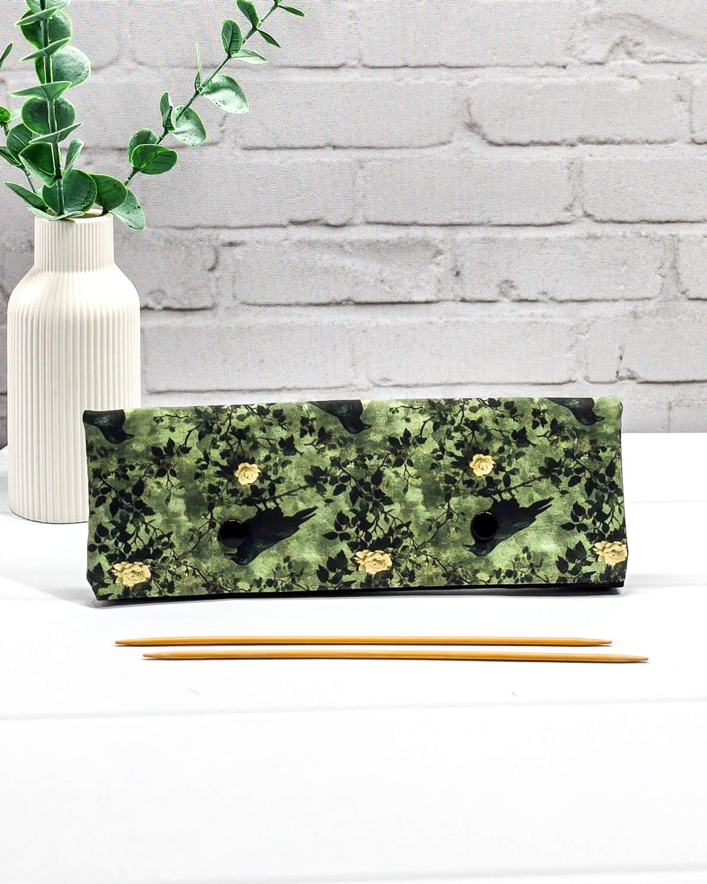 Lange grüne Nadelgarage mit Druckknöpfen, gemustert mit Raben und Rosen, passend für ein 20cm Nadelspiel zum Schutz von Strickmaschen. Handgenäht von Nadelmikado in Bayern.
