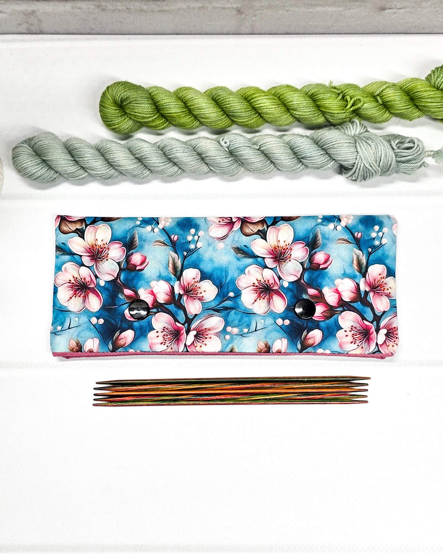 Nadelgarage für 15cm Nadelspiele mit rosa Kirschblütenmotiv auf blauem Grund und zwei schwarzen Druckknöpfen. Handgenäht in Bayern von Nadelmikado.