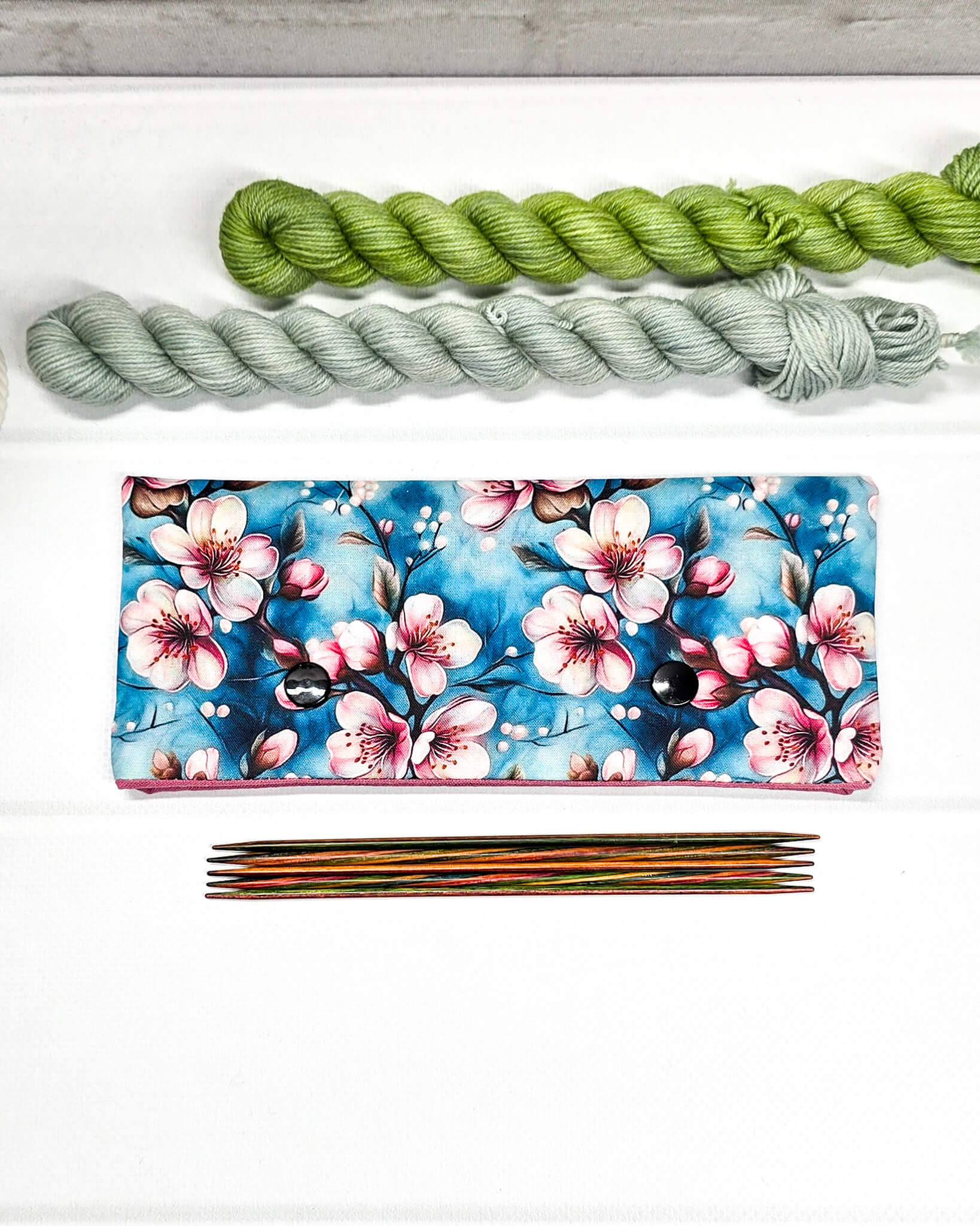 Nadelgarage für 15cm Nadelspiele mit rosa Kirschblütenmotiv auf blauem Grund und zwei schwarzen Druckknöpfen. Handgenäht in Bayern von Nadelmikado.