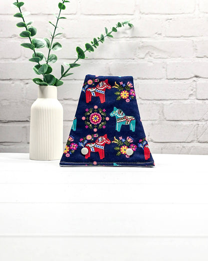 Nadelgarage für Trio-Stricknadeln aus dunkelblauem Stoff mit bunten Dala-Pferden, Blumenmotiven und zwei hellen Druckknöpfen. Handgenäht in Bayern von Nadelmikado.