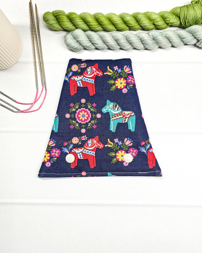 Nadelgarage für Trio-Stricknadeln aus dunkelblauem Stoff mit bunten Dala-Pferden, Blumenmotiven und zwei hellen Druckknöpfen. Handgenäht in Bayern von Nadelmikado.