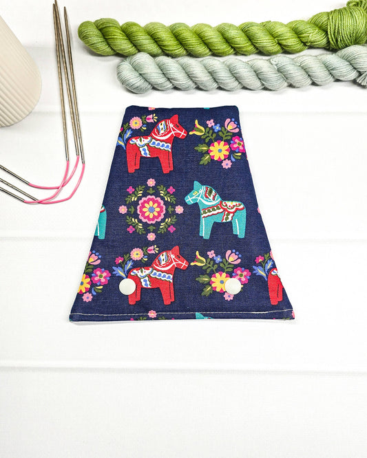 Nadelgarage für Trio-Stricknadeln aus dunkelblauem Stoff mit bunten Dala-Pferden, Blumenmotiven und zwei hellen Druckknöpfen. Handgenäht in Bayern von Nadelmikado.