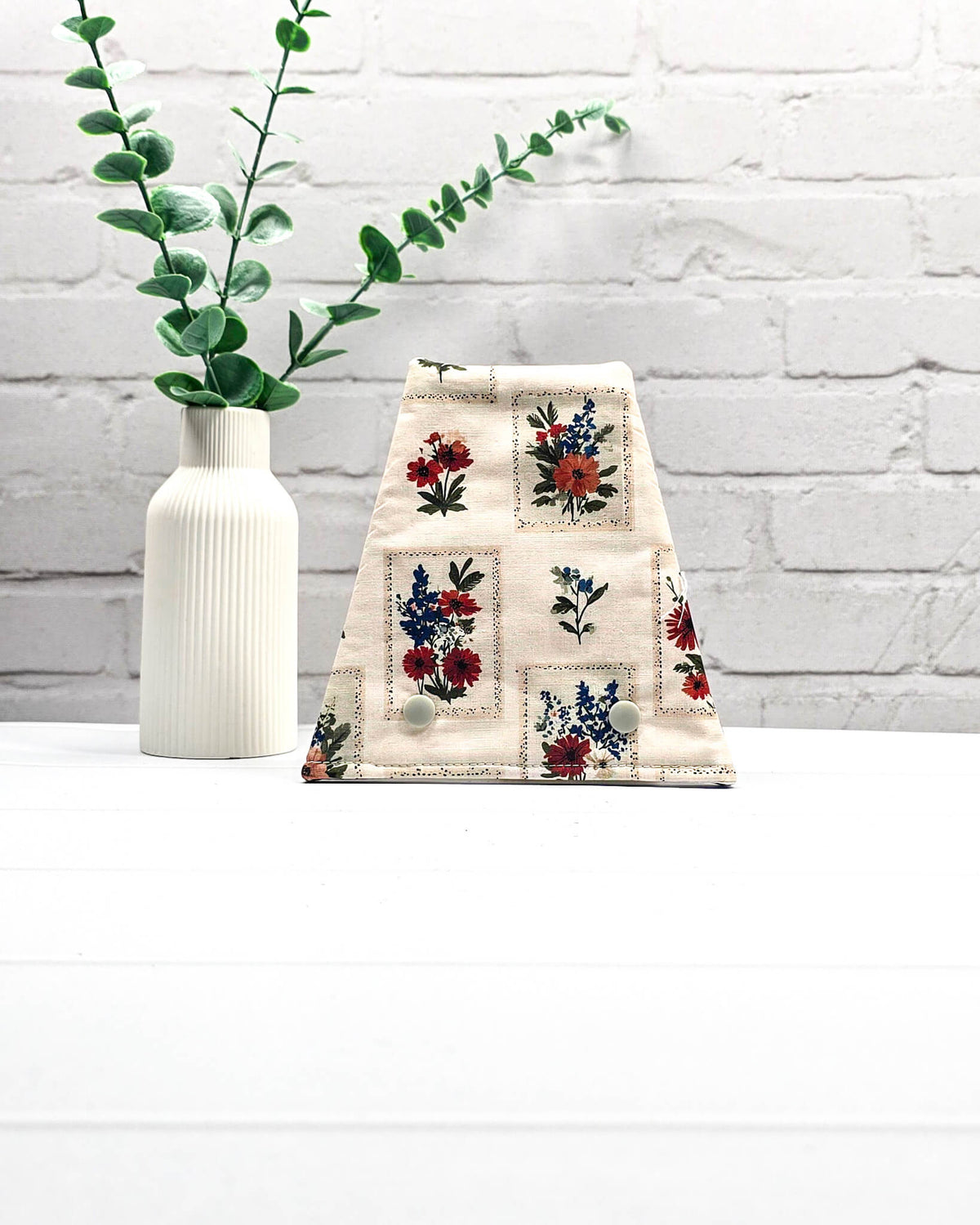 Nadelgarage für Trio-Stricknadeln aus hellem Stoff mit kleinen floralen Motiven in Rot, Blau und Orange sowie zwei hellen Druckknöpfen. Handgenäht in Bayern von Nadelmikado.