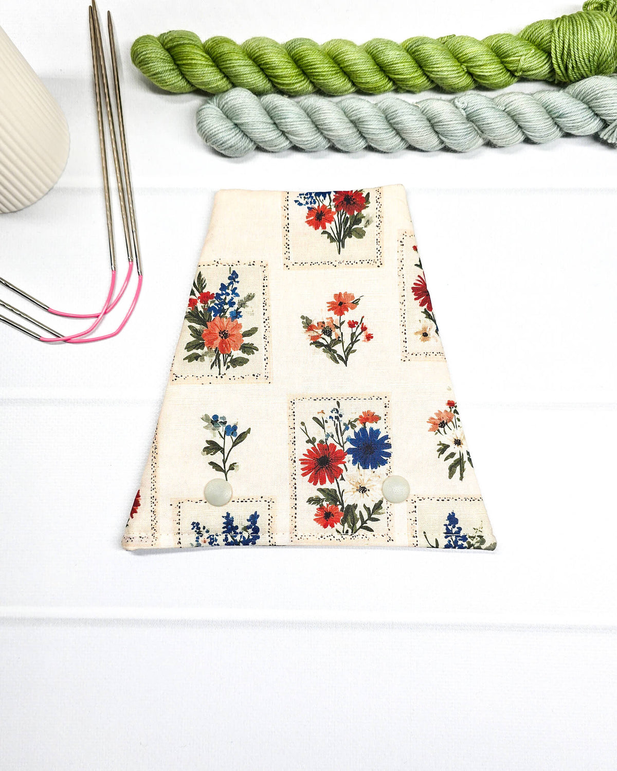 Nadelgarage für Trio-Stricknadeln aus hellem Stoff mit kleinen floralen Motiven in Rot, Blau und Orange sowie zwei hellen Druckknöpfen. Handgenäht in Bayern von Nadelmikado.