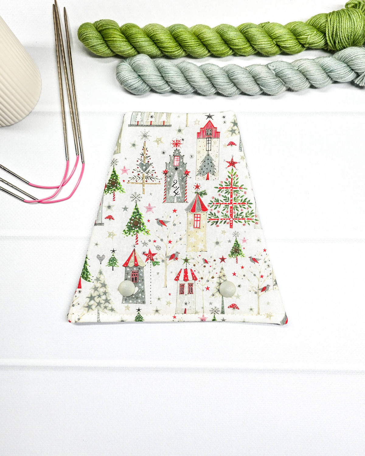 Nadelgarage für Trio-Stricknadeln mit weihnachtlichen Häusern, Tannenbäumen und Sternen auf weißem Stoff und zwei Druckknöpfen. Handgenäht in Bayern von Nadelmikado.