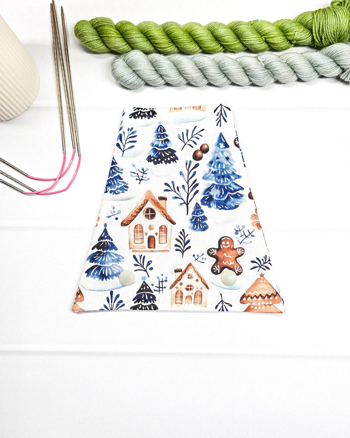 Nadelgarage für Trio-Stricknadeln aus weißem Stoff mit blauen Tannenbäumen, kleinen Häusern, Lebkuchenfigur und zwei hellen Druckknöpfen. Handgenäht in Bayern von Nadelmikado.