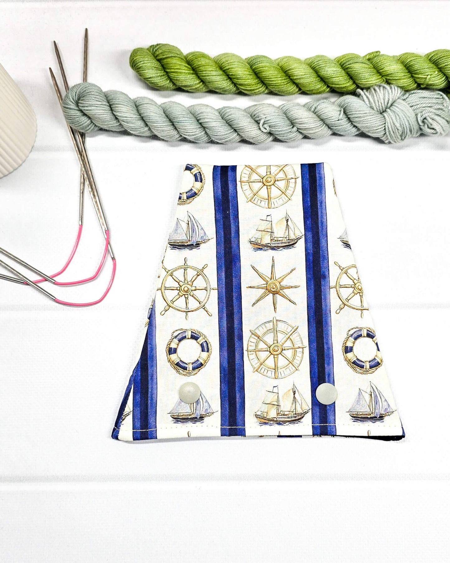 Nadelgarage für Trios aus cremeweißem Stoff mit blauen Streifen, goldenen Steuerrädern, Segelschiffen und zwei hellen Druckknöpfen. Handgenäht in Bayern von Nadelmikado. 