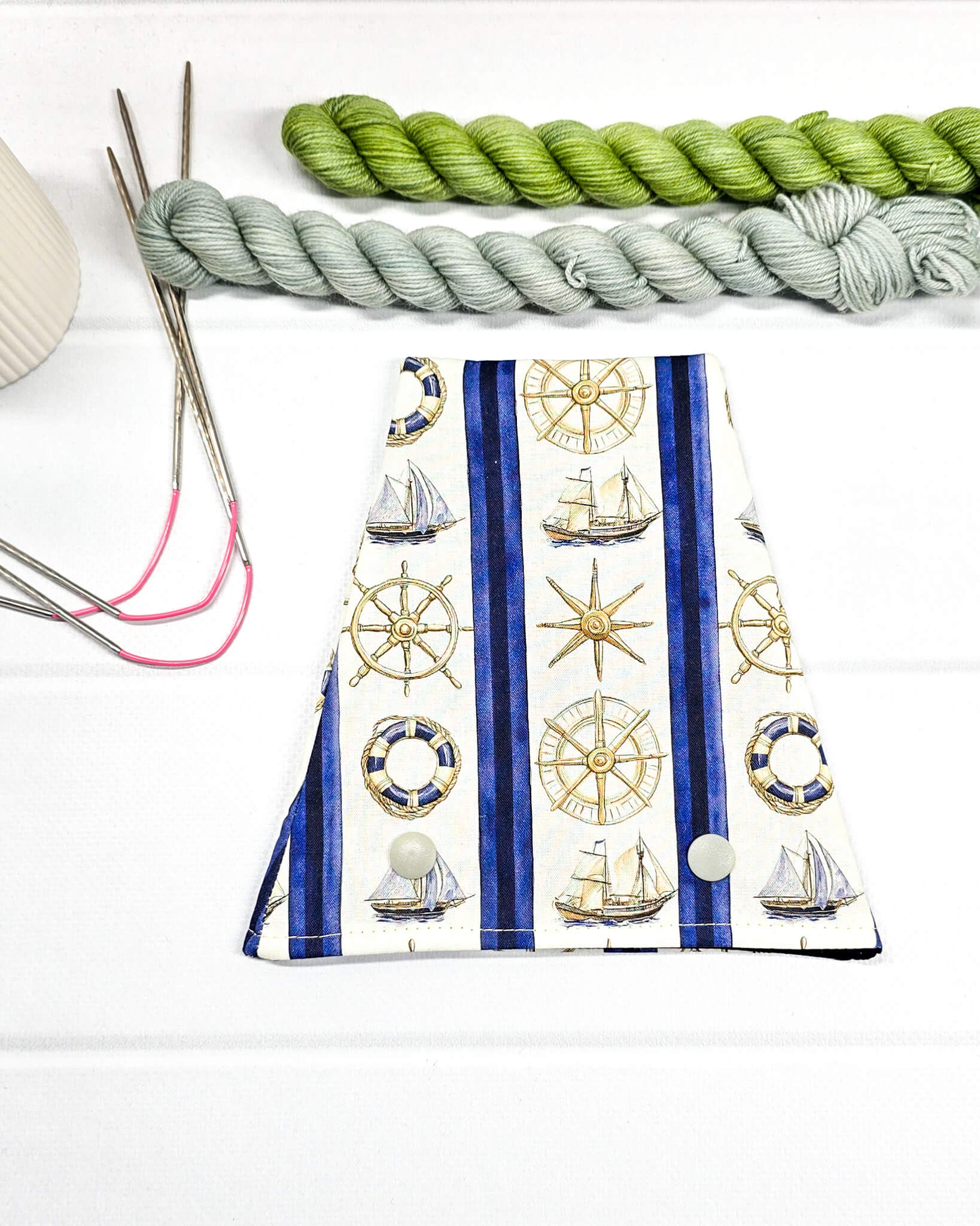 Nadelgarage für Trios aus cremeweißem Stoff mit blauen Streifen, goldenen Steuerrädern, Segelschiffen und zwei hellen Druckknöpfen. Handgenäht in Bayern von Nadelmikado. 
