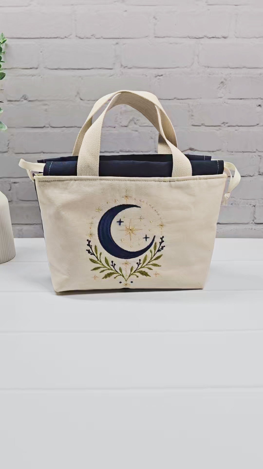 Projekttasche Alva S aus hellem Canvas mit Stickmotiv blaue Mondsichel und Sterne, Henkeln und dunkelblauem Kordelzug. Handgenäht in Bayern von Nadelmikado.