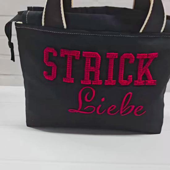 Projekttasche Alva S aus schwarzem Canvas mit rot gesticktem 3D-Schriftzug Strickliebe, Henkeln und Kordelzugkragen. Handgenäht in Bayern von Nadelmikado.
