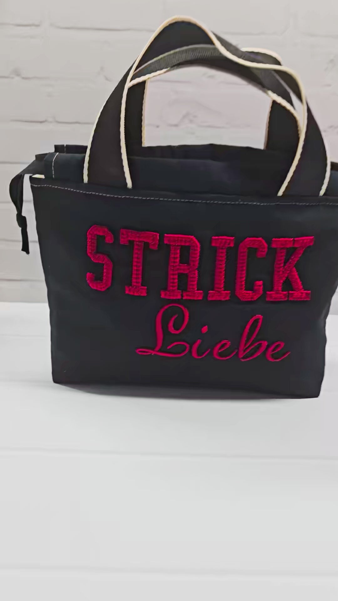 Projekttasche Alva S aus schwarzem Canvas mit rot gesticktem 3D-Schriftzug Strickliebe, Henkeln und Kordelzugkragen. Handgenäht in Bayern von Nadelmikado.