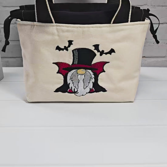 Projekttasche Alva S aus hellem Canvas mit gesticktem Vampir-Wichtel und Fledermäusen, Henkeln und schwarzem Kordelzug. Handgenäht in Bayern von Nadelmikado.