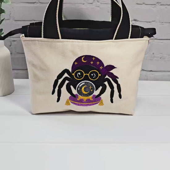Projekttasche Alva S aus hellem Canvas mit gestickter Wahrsager Spinne und Kristallkugel, Henkeln und schwarzem Kordelzugkragen. Handgenäht in Bayern von Nadelmikado.