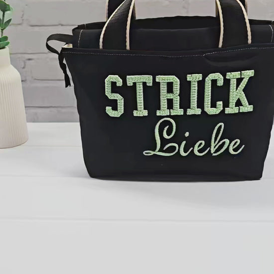 Projekttasche Alva S aus schwarzem Canvas mit mintgrüner 3D-Stickerei Strickliebe, Henkeln und schwarzem Kordelzugkragen. Handgenäht in Bayern von Nadelmikado.