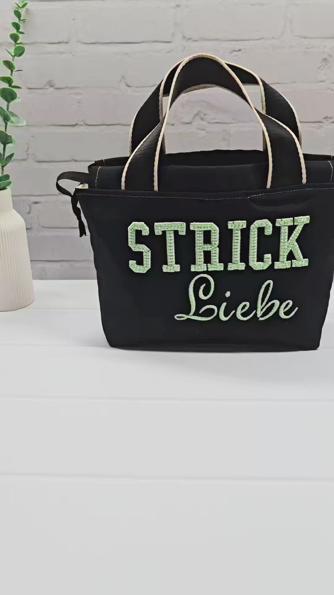Projekttasche Alva S aus schwarzem Canvas mit mintgrüner 3D-Stickerei Strickliebe, Henkeln und schwarzem Kordelzugkragen. Handgenäht in Bayern von Nadelmikado.