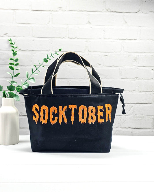 Bestickter Projektbeutel Alva S aus schwarzem Canvas mit orangefarbenem Socktober-Schriftzug, handgenäht in Bayern von NadelMikado