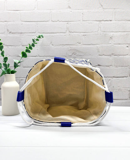 Projektbeutel Aska M aus blau-weiß quergestreiftem Stoff mit kleinen Muschelmotiven, zwei seitlich herausgeführten, hellen Kordeln und einer blauen Schlaufe an der Oberkante. Rice Bag. Handgenäht in Bayern von Nadelmikado. 