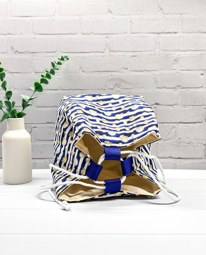 Projektbeutel Aska M aus blau-weiß quergestreiftem Stoff mit kleinen Muschelmotiven, zwei seitlich herausgeführten, hellen Kordeln und einer blauen Schlaufe an der Oberkante. Rice Bag. Handgenäht in Bayern von Nadelmikado. 