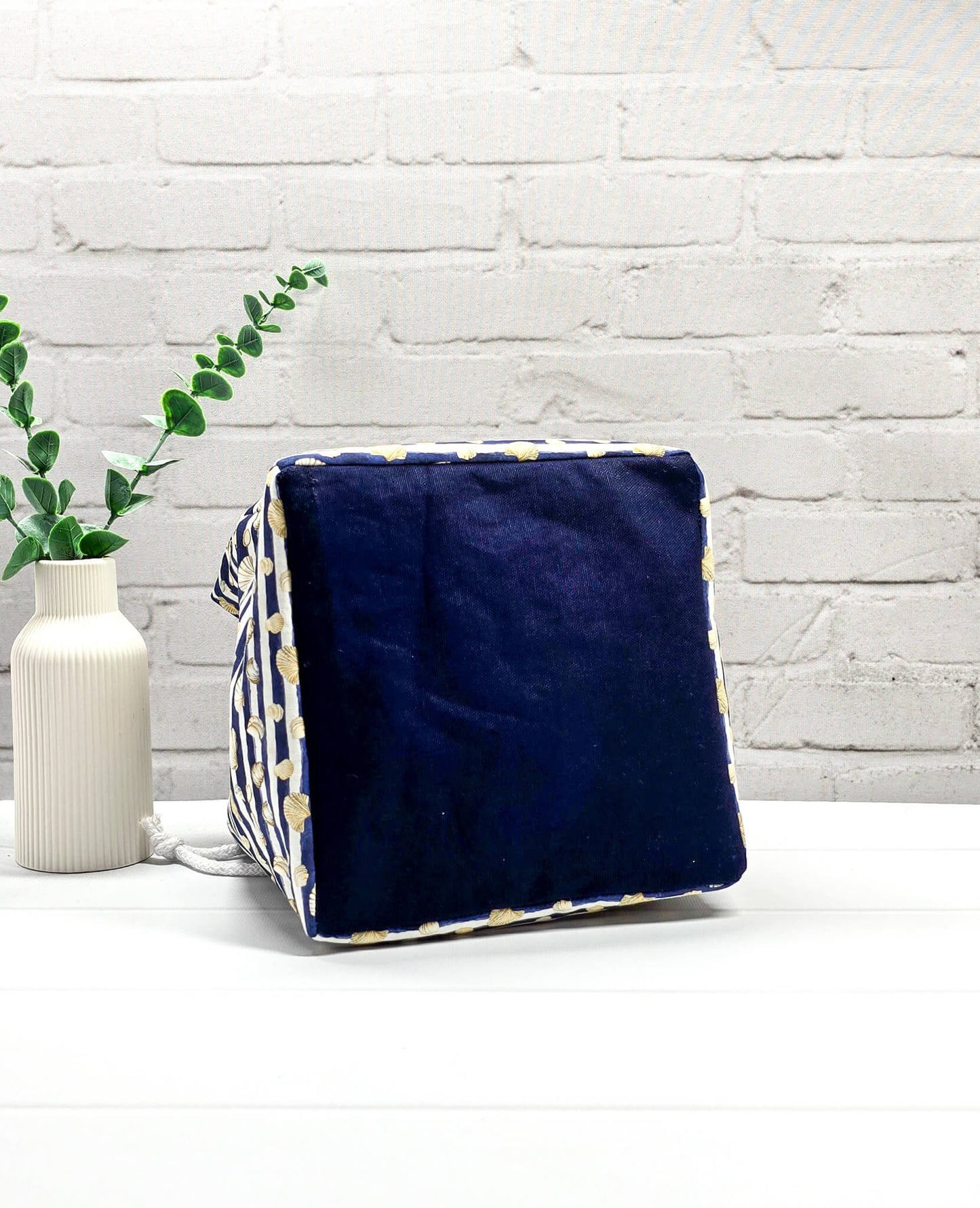 Projektbeutel Aska M aus blau-weiß quergestreiftem Stoff mit kleinen Muschelmotiven, zwei seitlich herausgeführten, hellen Kordeln und einer blauen Schlaufe an der Oberkante. Rice Bag. Handgenäht in Bayern von Nadelmikado. 
