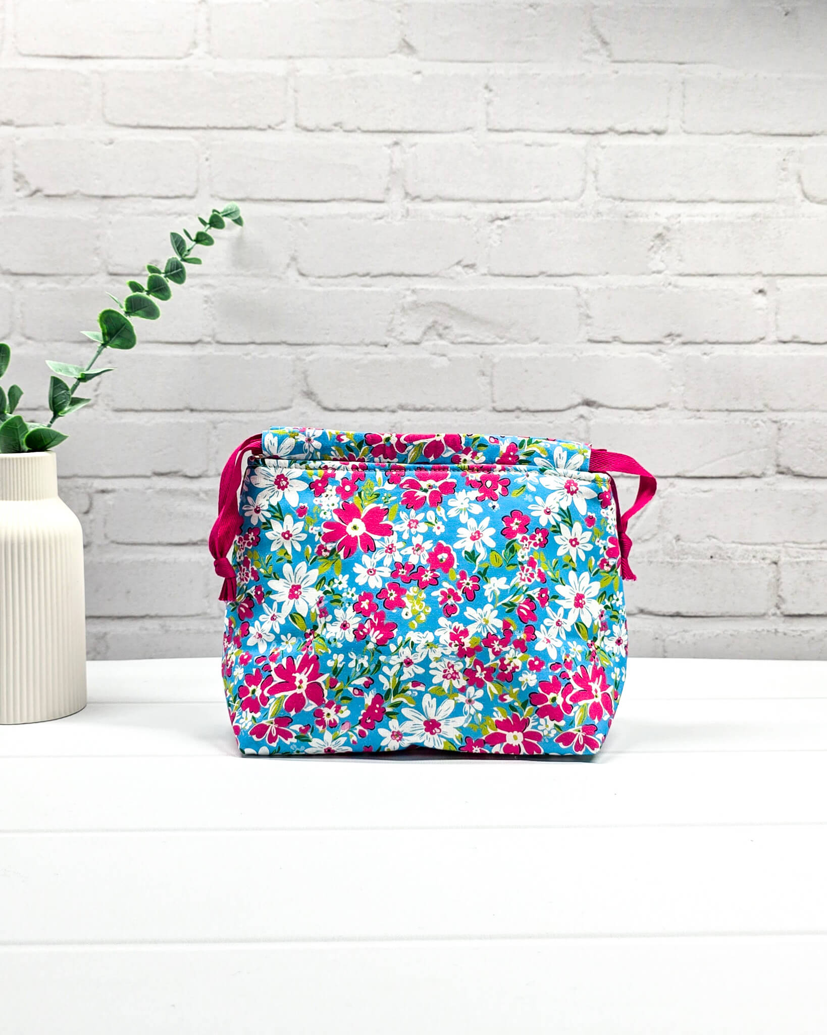 Projektbeutel Lyra mit pinken und weißen Blumen auf türkisfarbenem Grund und mit pinkem Kordelzug. Handgenäht in Bayern von Nadelmikado 