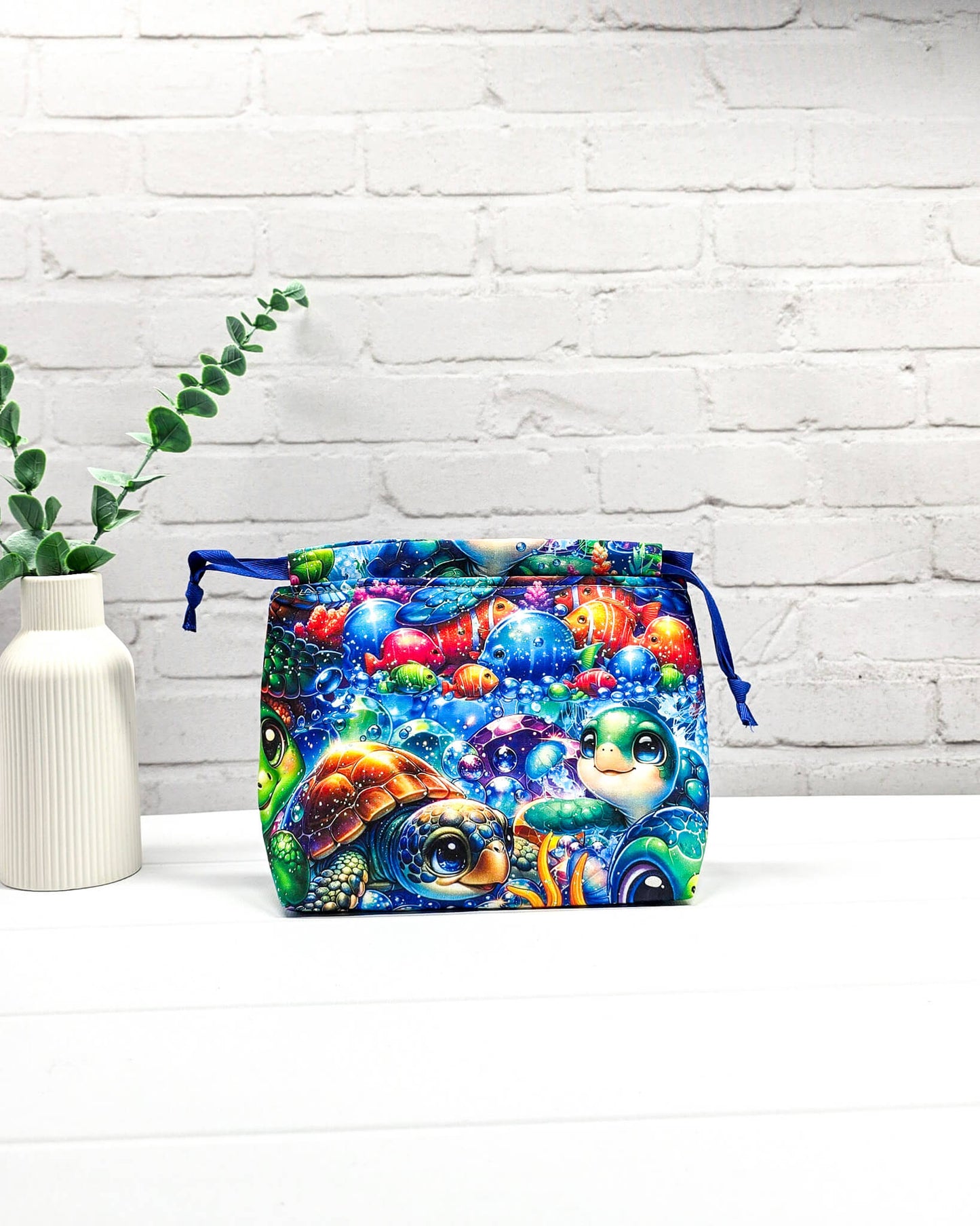 Projektbeutel Lyra mit einem bunten Motiv aus Meeresschildkröten und Fischen unter Wasser sowie blauem Kordelzug. Handgenäht in Bayern von Nadelmikado. 