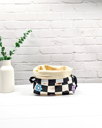 Projektbeutel Lyra bedruckt mit einem schwarz-weißen Schachbrettmuster und bunten, einfachen Blumenblüten sowie schwarzen Kordelzügen. Handgenäht in Bayern von Nadelmikado. 