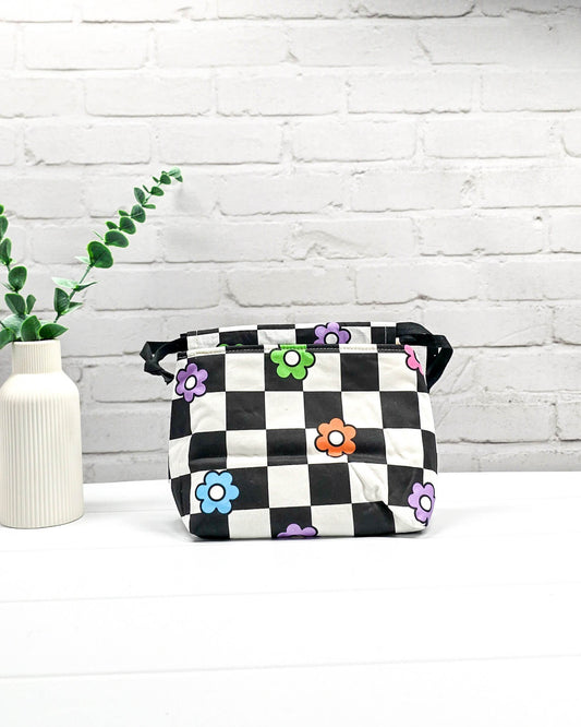 Projektbeutel Lyra bedruckt mit einem schwarz-weißen Schachbrettmuster und bunten, einfachen Blumenblüten sowie schwarzen Kordelzügen. Handgenäht in Bayern von Nadelmikado. 