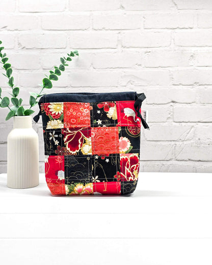 Projektbeutel Tindra bedruckt mit einem roten und schwarzen Patchwork-Muster aus Kranichen und Blumenblüten sowie schwarzen Kordelzügen. Handgenäht in Bayern von Nadelmikado. 