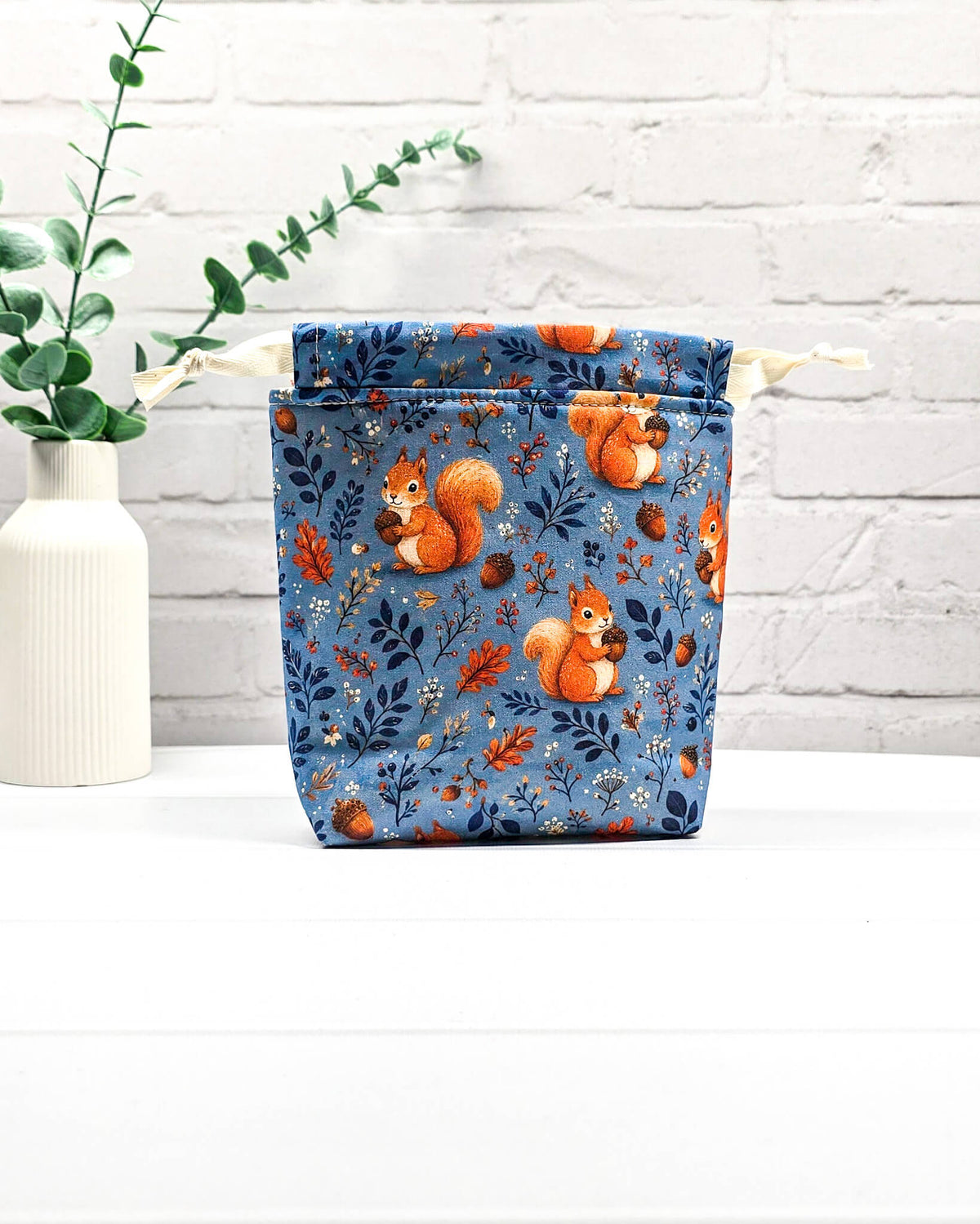 Kleiner Projektbeutel Tindra mit Tunnelzug aus blauem Baumwollstoff mit orangefarbenen Eichhörnchen, Eicheln und Blättern für Strickprojekte bis 50 g Wolle. Handgenäht in Bayern von Nadelmikado.