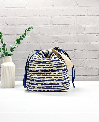 Projektbeutel Tuva S aus blau-weiß quergestreiftem Stoff mit kleinen Muschelmotiven, einer hellen Gurtband-Schlaufe und dunkelblauem Kordelzug. Handgenäht in Bayern von Nadelmikado. 