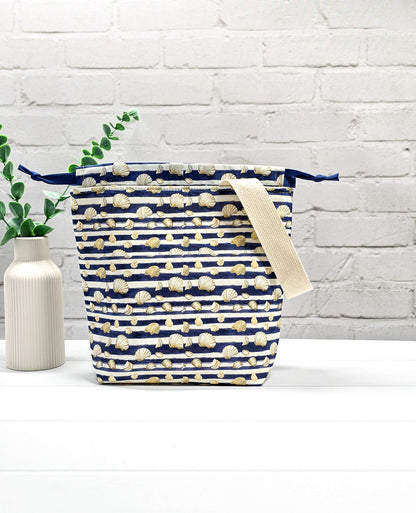 Projektbeutel Tuva S aus blau-weiß quergestreiftem Stoff mit kleinen Muschelmotiven, einer hellen Gurtband-Schlaufe und dunkelblauem Kordelzug. Handgenäht in Bayern von Nadelmikado. 