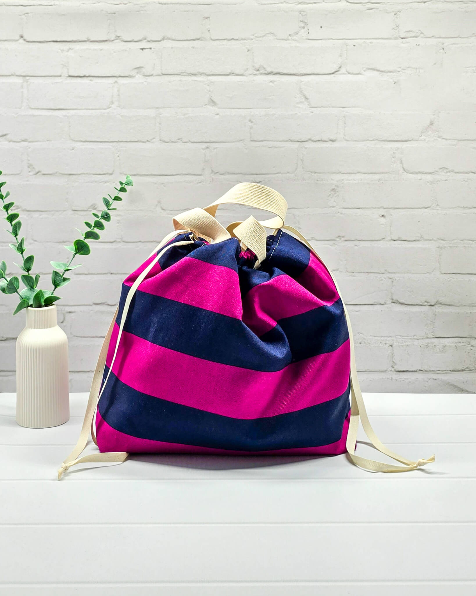 Projekttasche Alva L mit breiten horizontalen Streifen in Fuchsia und Dunkelblau, zwei hellen Tragehenkeln und einem Kordelzugverschluss. Handgenäht in Bayern von Nadelmikado. 