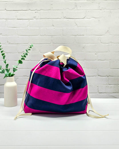 Projekttasche Alva L mit breiten horizontalen Streifen in Fuchsia und Dunkelblau, zwei hellen Tragehenkeln und einem Kordelzugverschluss. Handgenäht in Bayern von Nadelmikado. 