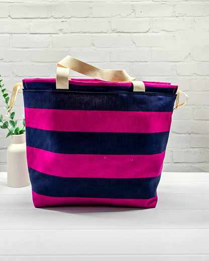 Projekttasche Alva L mit breiten horizontalen Streifen in Fuchsia und Dunkelblau, zwei hellen Tragehenkeln und einem Kordelzugverschluss. Handgenäht in Bayern von Nadelmikado. 